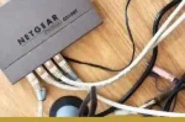 A switch with various network cables tangled on a wooden surface for Subnetting, branded with the NetworkUstad logo