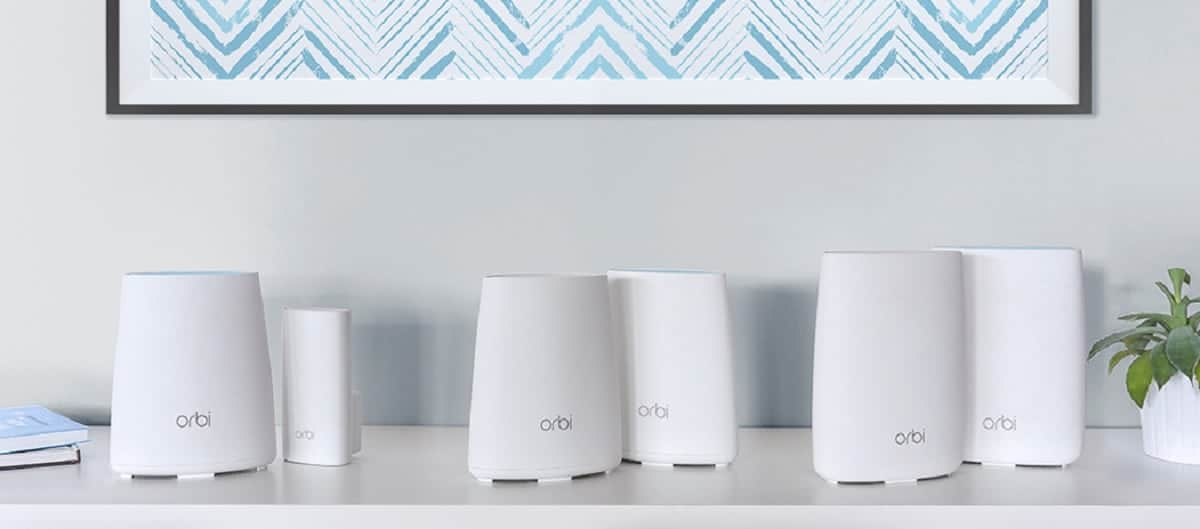 A lineup of five white Orbi router increasing in size on a wooden table, illustrating various models available.