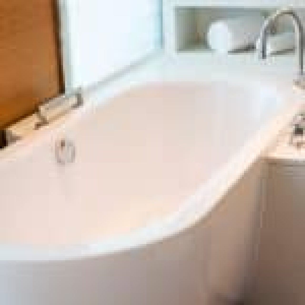 A modern, clean white bathtub with a sleek silver faucet, set against a wooden wall and white countertop.