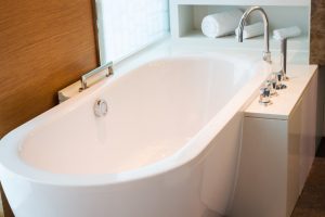 A modern, clean white bathtub with a sleek silver faucet, set against a wooden wall and white countertop.
