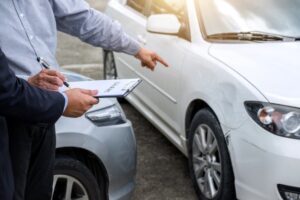 Person filing a car accident claim by pointing at vehicle damage while holding paperwork.