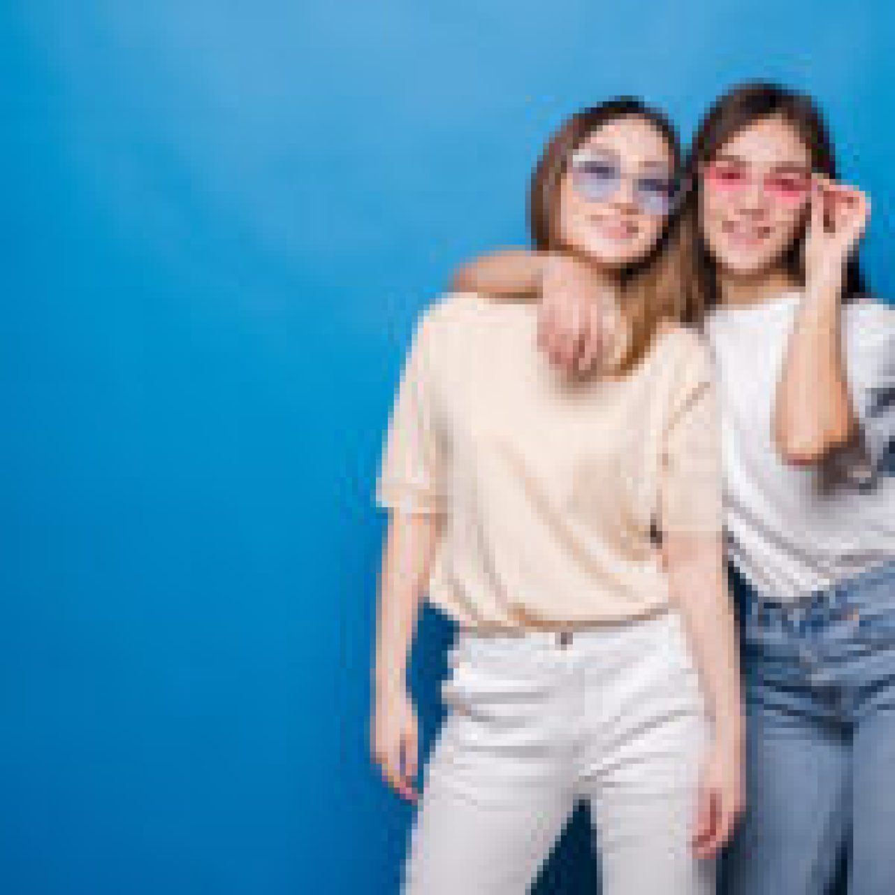 Two people posing against a blue background, wearing casual outfits and sunglasses.
