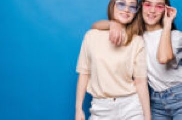 Two people posing against a blue background, wearing casual outfits and sunglasses.