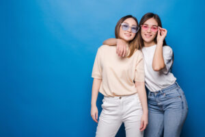 Two people posing against a blue background, wearing casual outfits and sunglasses.