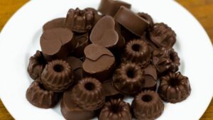 A close-up of homemade chocolate bars with nuts and fruits on a wooden cutting board.