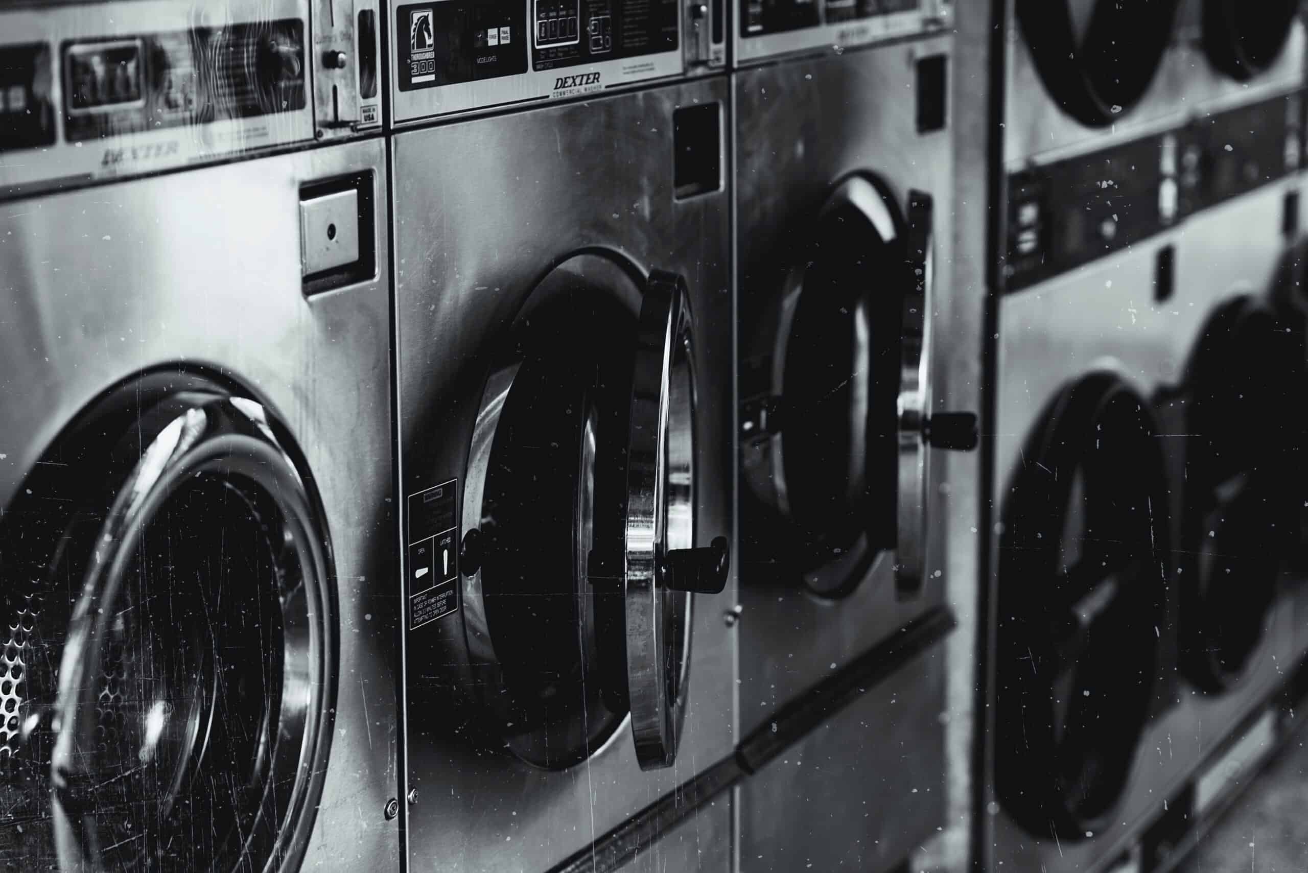 Row of modern semi-automatic washing machines in grayscale.