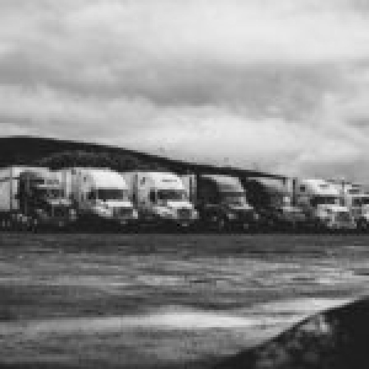 A monochrome photo of multiple trucks parked at a rest area under an overcast sky, symbolizing road safety through vehicle technology.