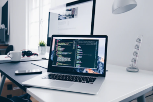 Workspace with a laptop displaying code, smartphone, headphones, potted plant, and a desk lamp, symbolising web portal design.