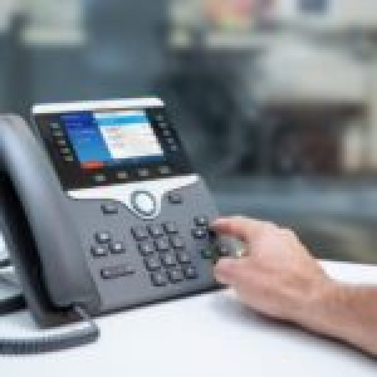 Person dialing a number on a VoIP phone with a digital display screen.