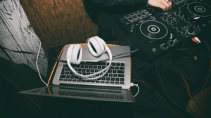 A DJ’s laptop with white headphones and mixing console, symbolizing professional ambient commercial music services.