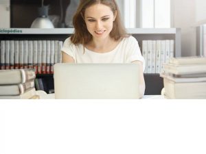 Student studying at a laptop with stacks of books on either side, symbolizing focused learning.