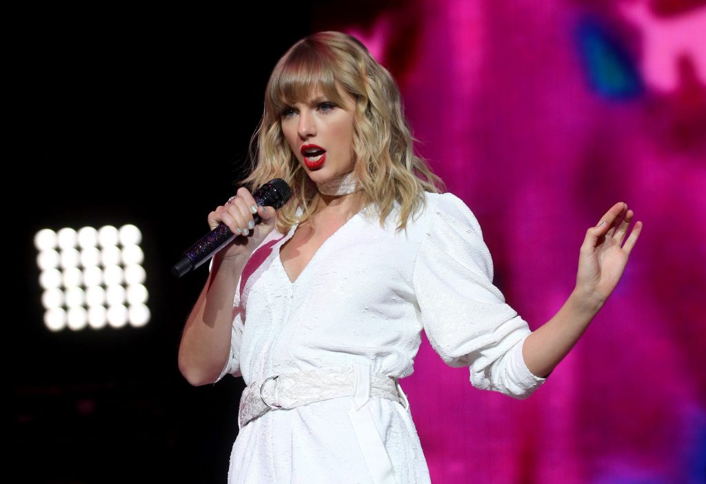 A person on stage singing into a microphone with stage lighting in the background and their face obscured for privacy.”