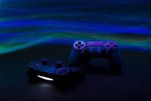 Two gaming controllers under blue ambient lighting with vibrant green and blue wave patterns in the background.