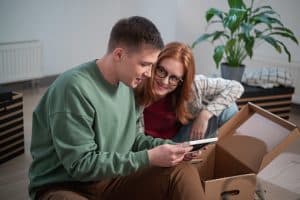 Two people examining documents from an open cardboard box, with a plant in the background.