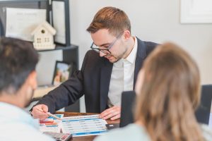 Three people sitting around a table, discussing a document with colorful charts and data, indicating a business meeting or consultation.
