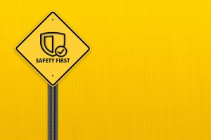 A yellow diamond-shaped ‘SAFETY FIRST’ sign on a pole against a yellow background.