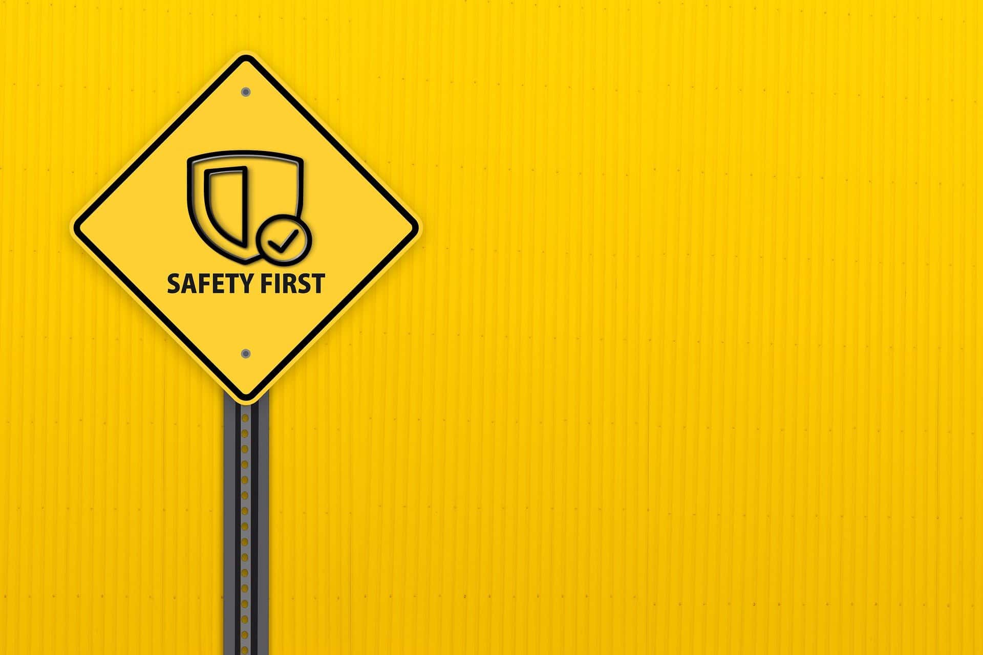 A yellow diamond-shaped ‘SAFETY FIRST’ sign on a pole against a yellow background.