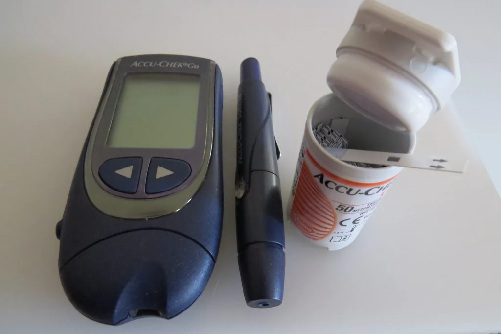 Blood glucose monitoring system with a digital screen, lancing device, and a bottle of test strips, used for checking blood sugar levels at home.