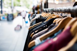 A variety of colorful garments displayed on wooden hangers against a blurred outdoor market backdrop.