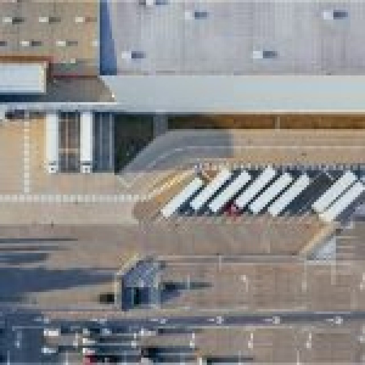 Aerial view of a logistics facility with multiple trucks parked in designated bays and cars in a parking lot.