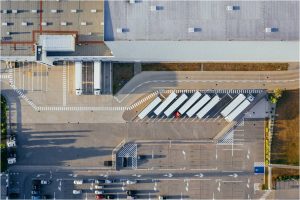 Aerial view of a logistics facility with multiple trucks parked in designated bays and cars in a parking lot.