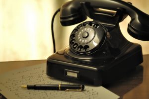 Vintage black rotary telephone on a handwritten notebook with a pen, symbolizing traditional communication methods.