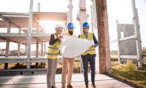 An architect reviewing blueprints on a table with a model home in the background.