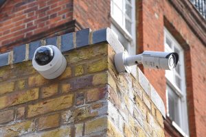 Two different styles of security cameras mounted on a brick wall corner of a building.
