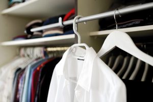 A white shirt on a hanger in the foreground with various clothes hanging in the background.