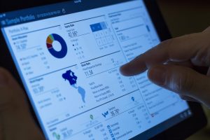Investment Portfolio : A close-up of a hand interacting with a financial portfolio dashboard on a tablet screen, displaying various graphs and statistics.