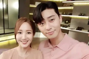 Park Seo Joon smiling with a woman in a pastel outfit during a 2025 brand event selfie, surrounded by shelves of shoes and bags, hinting at his endorsement career.
