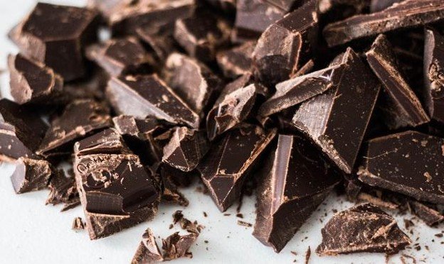 A close up image of several broken pieces of dark chocolate scattered on a light colored surface highlighting the texture and rich brown color of the chocolate chunks