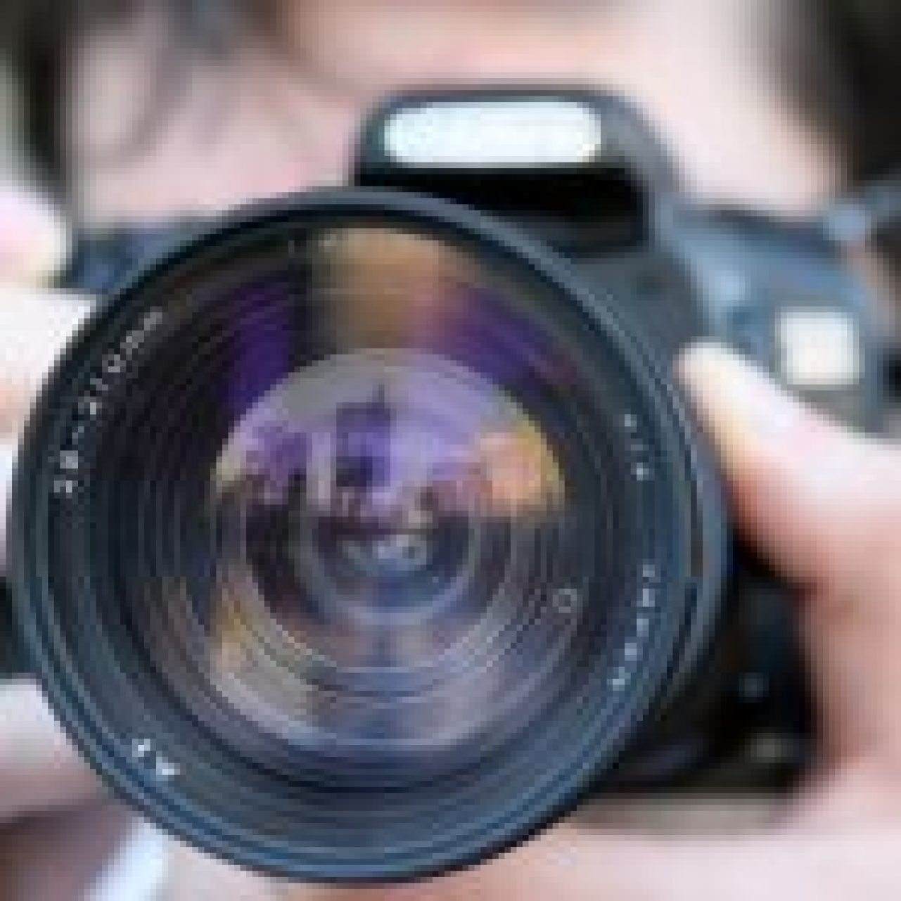 Photographer capturing cityscape reflected in camera lens.