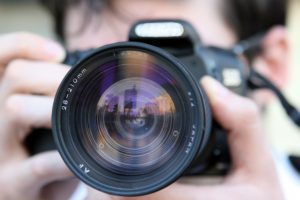 Photographer capturing cityscape reflected in camera lens.