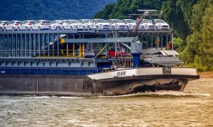 Cargo ship navigating a river with lush greenery on the banks.