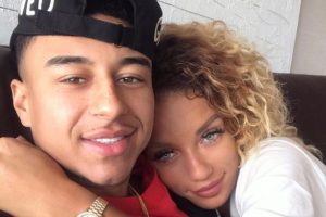 Close-up of two people holding hands with a blurred street scene in the background. Text overlay reads “Jena Frumes and Jesse Lingard: A Match Made in Heaven” and “The New Power Couple in Town