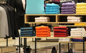 Assorted folded t-shirts in various colors neatly displayed on store shelves.