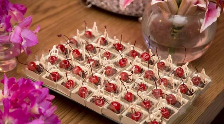 A tray of cherry topped desserts on a wooden table with pink flowers in the background