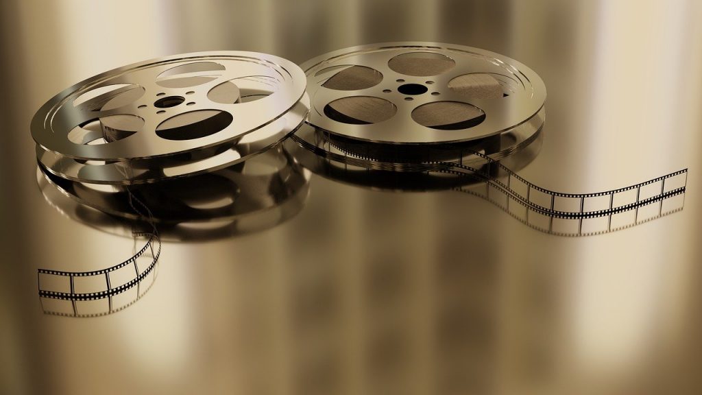 Two vintage film reels with filmstrip unraveled, resting on a reflective surface.