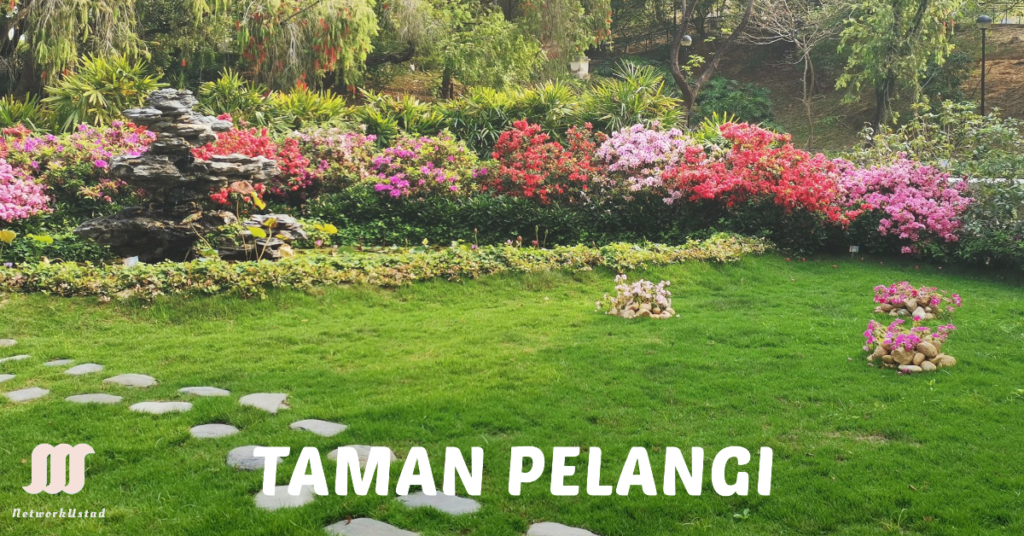 A vibrant garden with a variety of blooming flowers in shades of pink and red neatly trimmed grass and a stone pathway leading through it The garden is labeled TAMAN PELANGI in bold letters at the bottom with a logo consisting of three vertical lines on the left side