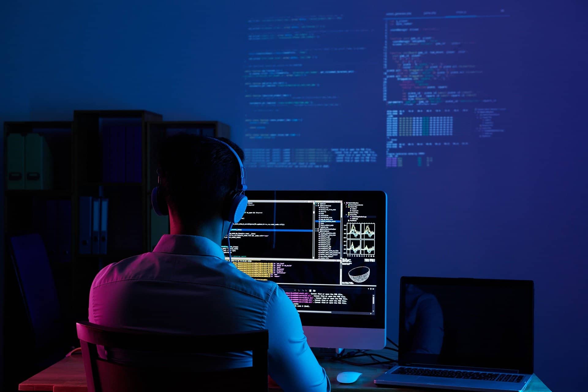 A programmer working on multiple monitors displaying code, symbolising the use of Microsoft Access in SMEs.