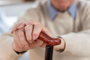 Close-up of an elderly person’s hands holding a wooden walking cane, symbolizing the need for support and stability. LoRa technology could enhance safety monitoring and assistance, improving their quality of life