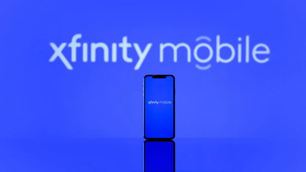 A smartphone with a blue screen displaying the logo ‘xfinity mobile’ is centered against a blue background with a larger, out-of-focus ‘xfinity mobile’ logo in the background.???