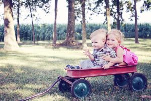 Two young children sitting in a red wagon in a park.