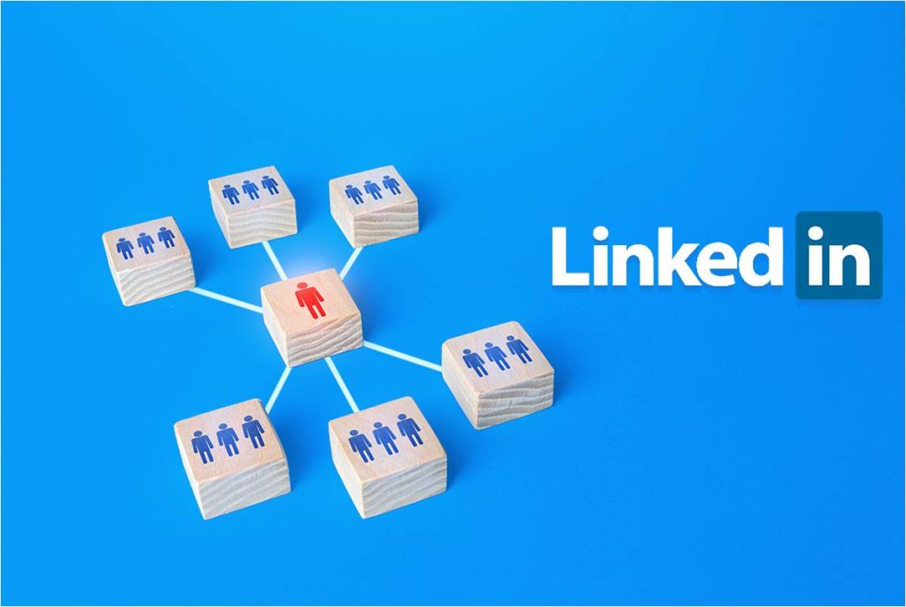 A graphic image featuring the LinkedIn logo on the upper right corner against a blue background In the center there are seven white cubes arranged in a hexagon pattern connected by lines Each cube has an icon of a person in blue except for one cube which has a red person icon This represents networking and connections within the professional platform LinkedIn highlighting one individual in red possibly as a focal point or standout profile within a network