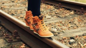 A pair of trendy tan-colored UGG boots with leopard print detail, worn while standing on railway tracks.