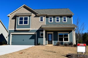 Two-story residential home with blue garage door and ‘UNDER CONTRACT’ sign on front lawn.