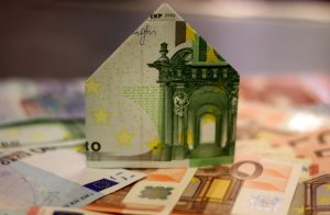 A creatively folded Euro banknote shaped like a house amidst various other Euro notes symbolizing real estate investment and financing.