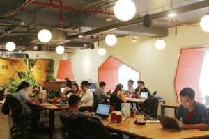 Professionals working in a well-lit coworking space with stylish wooden wall panels and hanging lights.