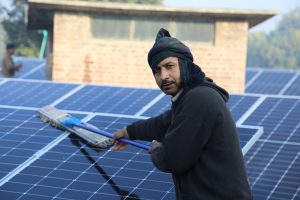 A worker cleaning solar panels with a squeegee to ensure efficient energy production.